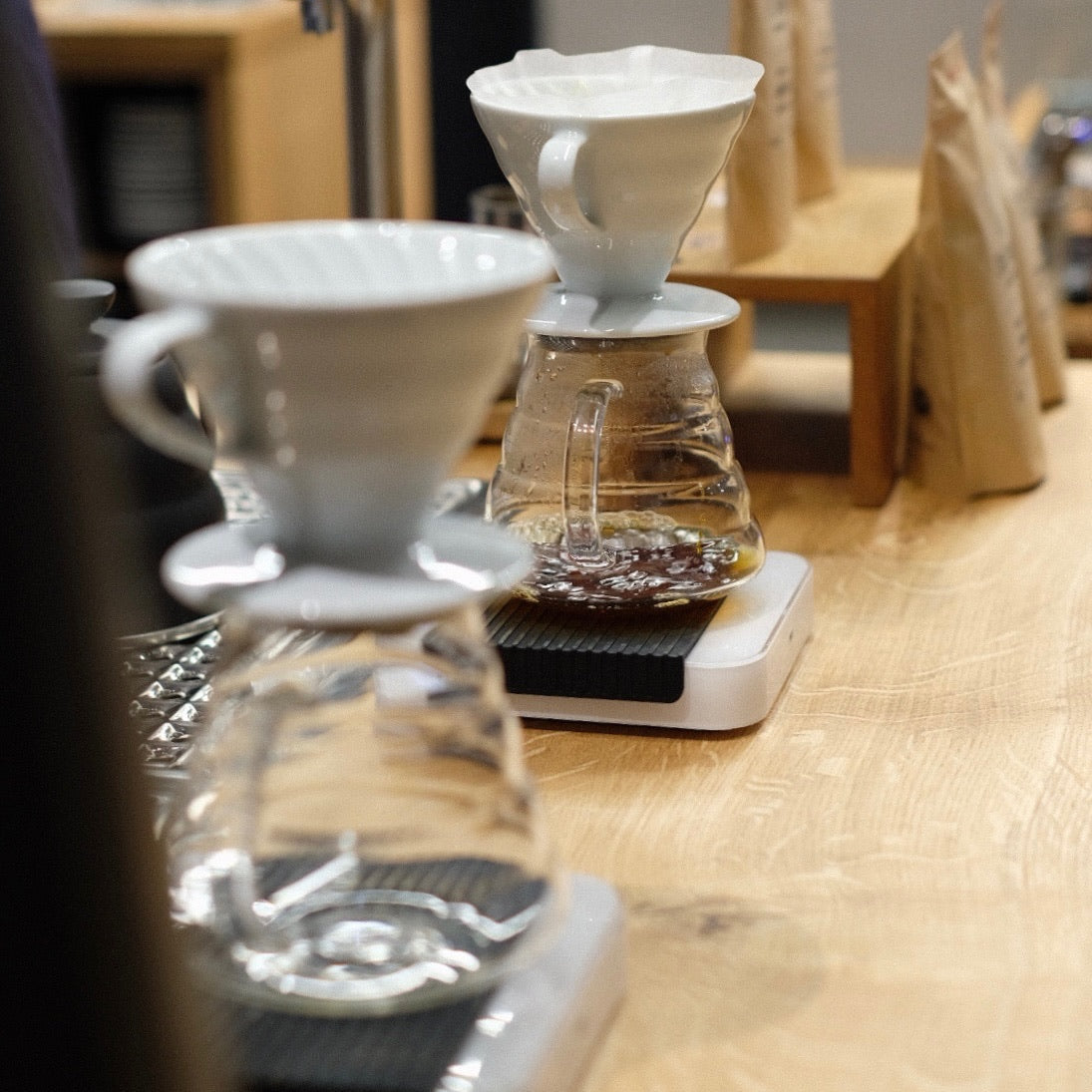 Brewing method showcasing JARDINES DEL EDEN PAPAYO coffee in glass pour-over vessels on a wooden counter.