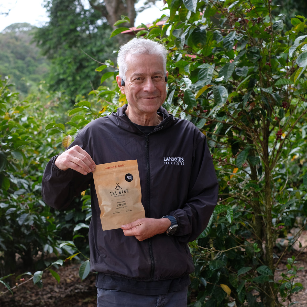 Person holding ELIDA GESHA NATURAL coffee packaging in a coffee plantation, showcasing Specialty Coffee Beans.