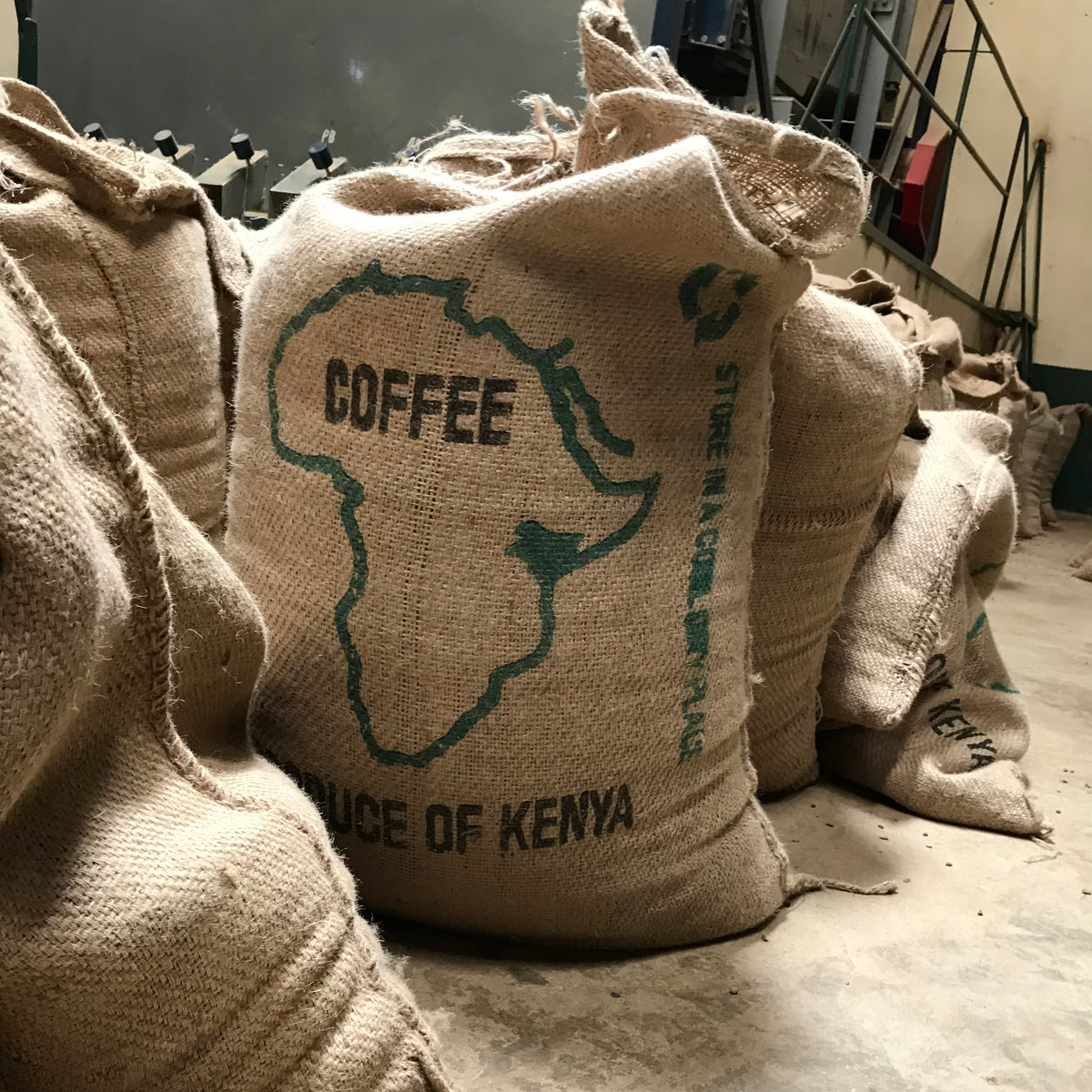 Burlap coffee bags with 'Coffee, Source of Kenya' text on a concrete floor.