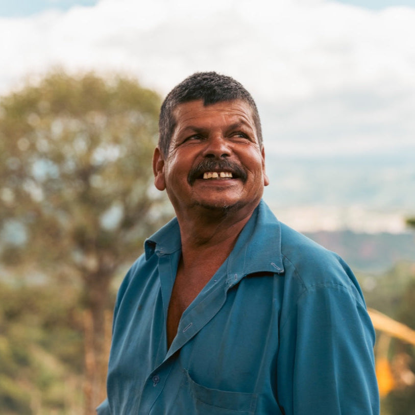 Coffee farmer wearing a blue shirt outdoors with trees and sky in the background