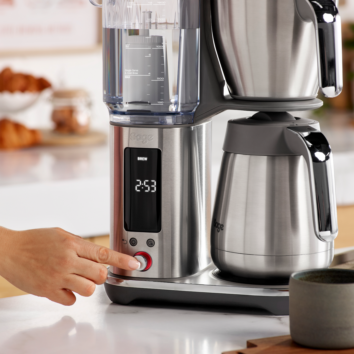 SAGE LUXE BREWER THERMAL coffee machine with a hand pressing the brew button, featuring a thermal carafe.