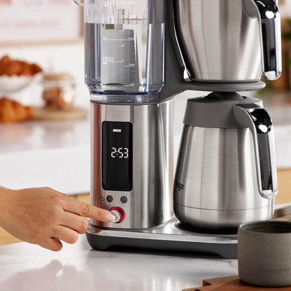 SAGE LUXE BREWER THERMAL coffee machine with a hand pressing the brew button, featuring a thermal carafe.