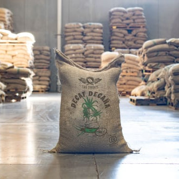 DECAF BALANCED coffee bag showcasing decaffeinated coffee in a warehouse full of coffee sacks.