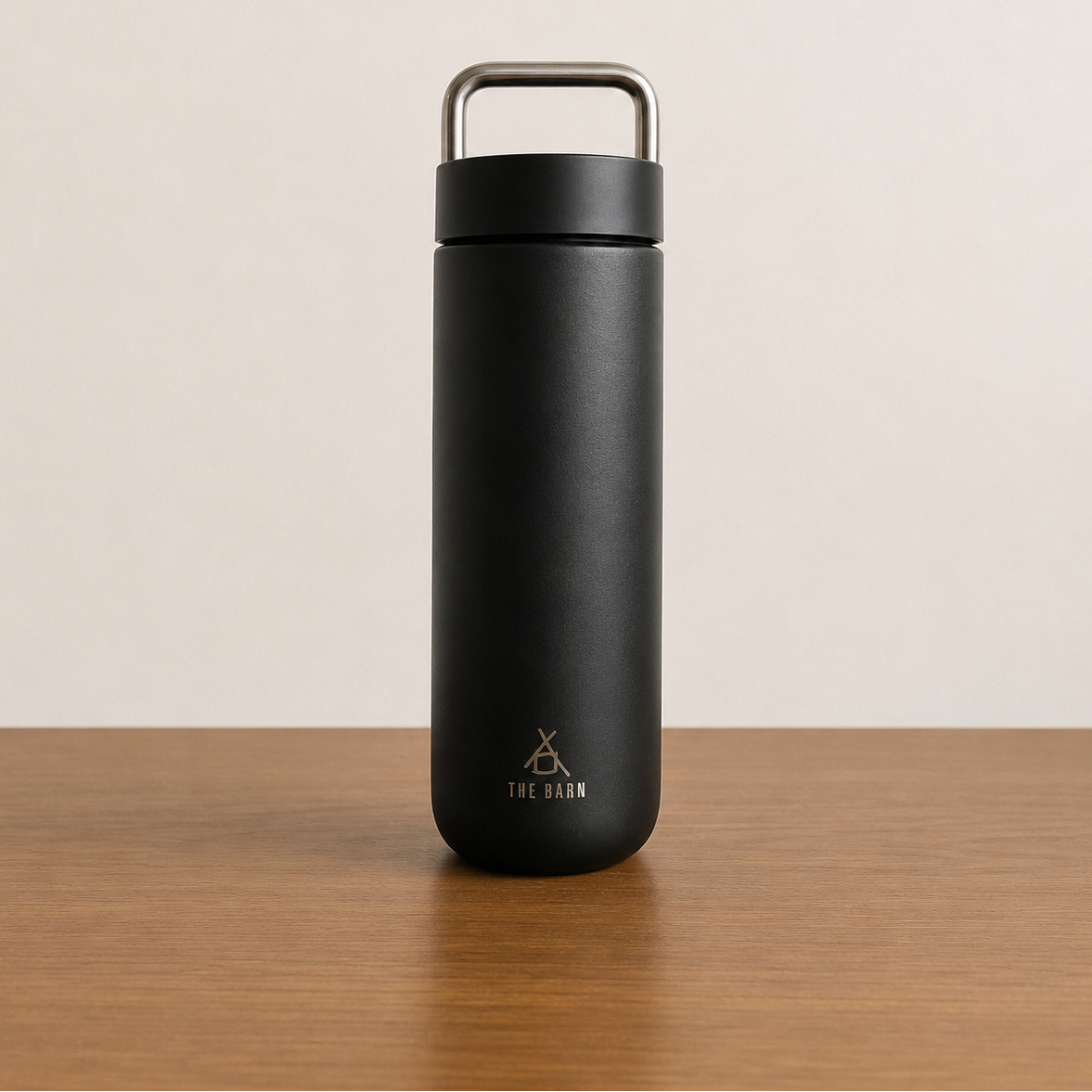 FELLOW CARTER CARRY TUMBLER in matte black with THE BARN engraving on a wooden table.