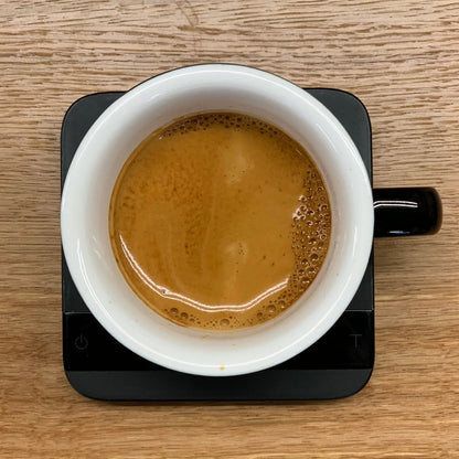 A close-up of a white cup of coffee on a black scale, representing the AUTUMN GIFT SUBSCRIPTION.